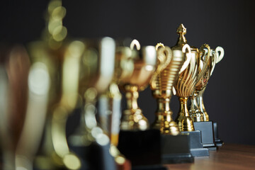 selective focus row of trophy on the wooden table against dark gray background - obrazy, fototapety, plakaty