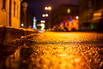 Autumn rainy night in the city. Empty street. Puddles on the road. Residential buildings in the city center. Colorful colors. Close up view from the curb level.