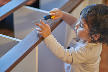 Son plays with screwdriver while his father assembles wooden furniture at home. Carpentry and parenting