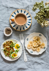 Delicious breakfast - coffee with cream, latkes, boiled eggs, micro greens, banana on a gray background, top view