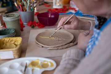 Senior female artist making flower ornament on ceramic product.