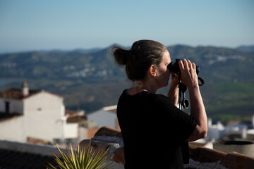 A woman is looking on the scenery with binoculars 