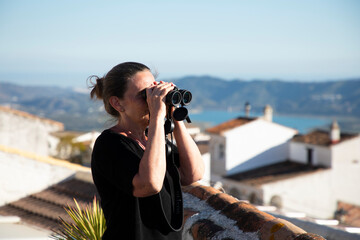 A woman is looking on the scenery with binoculars 