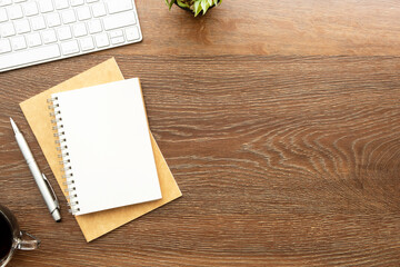Blank notebook with pen are on top of wood office desk table with computer tools, cup of coffee and supplies. Top view with copy space, flat lay.