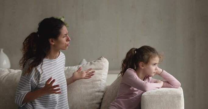 Irritated young mother scolds preschool kid girl for bad behavior and disobedience while sit on sofa, raising voice, scream at her little daughter. Difficulties of upbringing, misbehaved child concept