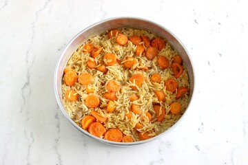 On a white marble table, cooked orzo pasta with sliced carrot and black pepper in a baking pan. Top view, selective focus