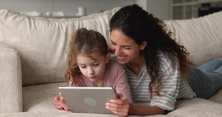 Young woman lying on sofa with daughter family use tablet wireless device choose goods and toys on web stores using retail services, buy video game for kid, cool application users, modern tech concept - Powered by Adobe