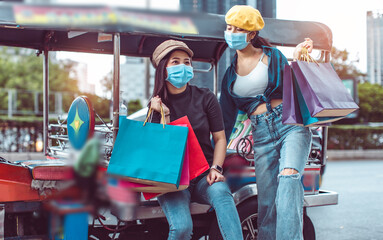 Asian woman wearing face mask. Happy woman with shopping bags.travel concept.group of happy friend are traveling.tourist holding shopping bag sitting in tuk tuk thai  taxi with blurring  town bangkok