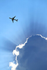 Silhouette of airplane flying in the blue cloudy sky with amazing sunbeams 