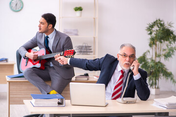 Young male employee playing guitar in the presence of old boss
