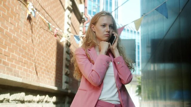 Good-looking young woman chatting on mobile phone with serious face then smiling in city on sunny summer day. Communication and youth concept.