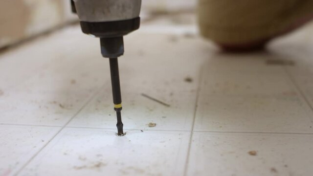 Man Using A Drill To Screw Into Vinyl Floor During A Bathroom Remodel