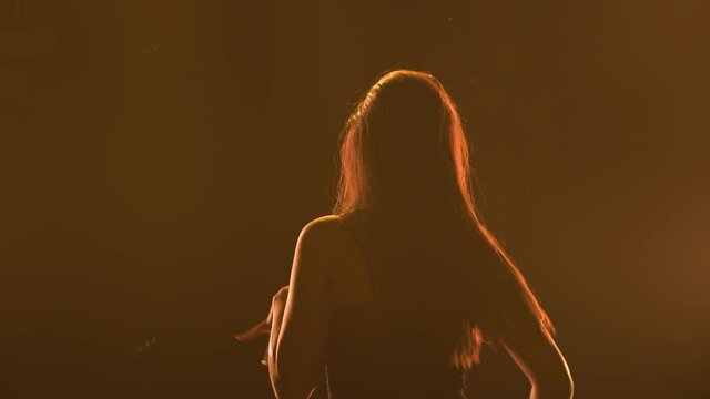 Silhouette of a sporty slender woman in black underwear dancing twerk in a dark studio with bright lights. The female dancer shakes her buttocks and seductively moves her half naked body. Close up.