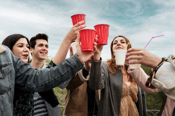 Outdoors friends party. Young people celebrating friendship toasting with beers in plastic ware red cup having fun and drinking together in the park