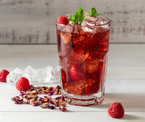 Cold sparkling hibiscus or karkade ice tea with lemon, mint, and raspberry in glass on a wooden...