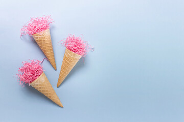 Simple summer composition with abstract ice cream waffle cones filled with shredded pink paper on blue background