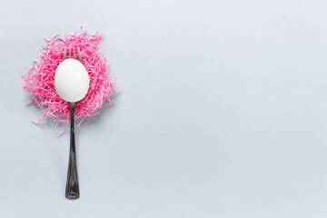 Simple Easter composition with a fork and white Easter egg on pink paper cloud on blue background