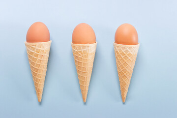 Easter composition with three waffle cones with three brown eggs on blue background