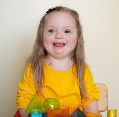 A beautiful girl with Down syndrome plays with a constructor, bright transparent figures, early...