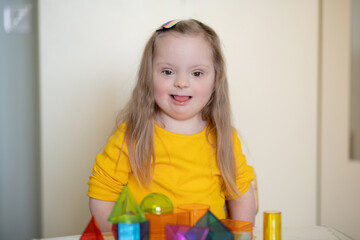 A beautiful girl with Down syndrome plays with a constructor, bright transparent figures, early...