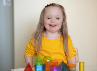 A beautiful girl with Down syndrome plays with a constructor, bright transparent figures, early...