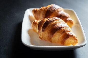 French croissant on white plate on black table background and nature sunlight with shadow through from window.