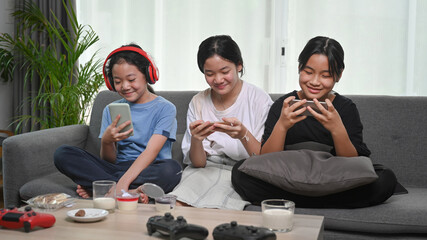 Three young asian girls using smart phone and sitting together on sofa at home.
