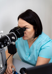 Fototapeta premium Health care, medicine, people, eyesight and technology concept. Female optician looks at special modern equipment for eye sigth testing. Closeup.