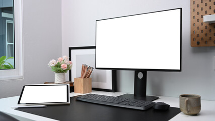 Contemporary workspace with computer, digital tablet and office supplies on white table.