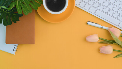 Stylish workspace with coffee cup, flowers, notebook and keyboard on yellow background.