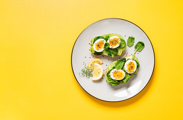 Healthy toast with sliced avocado, boiled eggs, spices and fresh spinach. Delicious breakfast or snack on yellow background. top view, space for text	
