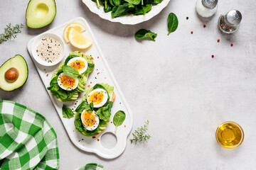 Healthy toast with sliced avocado, boiled eggs, spices and fresh spinach. Delicious breakfast or snack on gray stone background. top view, space for text	