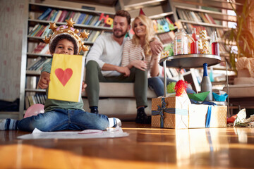 An adopted little boy showing his heart drawing at a kids birthday party in a cheerful atmosphere at home with his family. Family, celebration, together