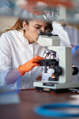 A young female student looking through a microscope in a laboratory. Science, chemistry, lab, people