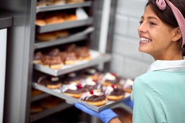 A young small business female owner in a candy workshop posing in front of the closet full of delicious handmade donuts. Pastry, dessert, sweet, making