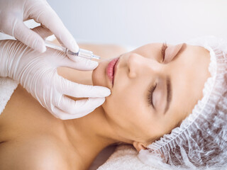 Beautician doing beauty procedure with syringe to face of young brunette woman in sunny spa center. Cosmetic medicine and surgery, beauty injections