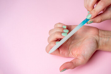 a woman herself is filing her nails with a nail file on her hand on a pink background. Hand nail care at home. Beauty and Health. Copy space