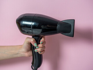 black hair dryer in a woman's hand on a pink background. Hair Care Product.