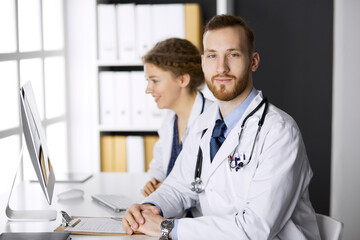 Male doctor withcolleague discussing current disease therapy while sitting at working place in...