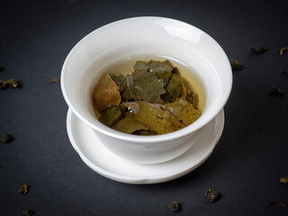 a white bowl with brewed tea leaves on a dark background. Close up, side view. Chinese tea, open leaves