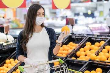 Woman wearing protective face mask and rubber glove holding orange at fruit grocery department store. shopping at supermarket in new normal lifestyle concept during Coronavirus