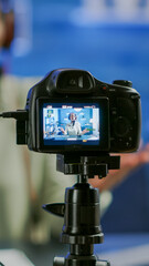 Close up of professional camera sitting in front of dslr recording online show. African woman vlogger speaking at microphone during livestreaming, blogger discussing in podcast wearing headphones