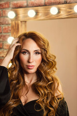 Fototapeta premium Portrait glam luxury redhead woman with curly hairstyle. Beautiful girl and long wavy hair. Beautiful sexy female model in black dress.