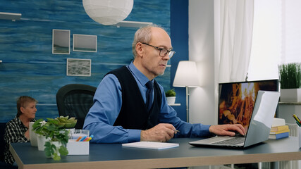 Middle age remote businessman working at laptop from home taking notes on notebook in modern living room. Busy focused employee using modern network technology reading writing, searching for job