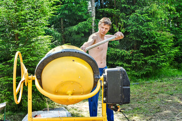 Production of concrete using a small concrete mixer. A young worker puts a shovel solution.