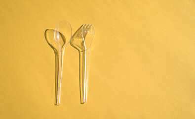 Transparent spoon and fork cutlery with shadows, on yellow background.
