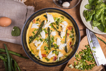 Cooking an omelet with asparagus, tomatoes and spinach - mixed eggs poured into a pan with asparagus, tomatoes and spinach, close-up