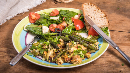American fried scrambled eggs with asparagus, spinach and tomatoes in a large plate on a rustic wooden table - a simple rustic breakfast
