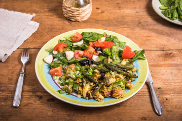 American fried scrambled eggs with asparagus, spinach and tomatoes in a large plate on a rustic wooden table - a simple rustic breakfast