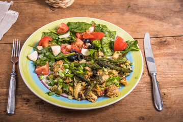 American fried scrambled eggs with asparagus, spinach and tomatoes in a large plate on a rustic wooden table - a simple rustic breakfast
